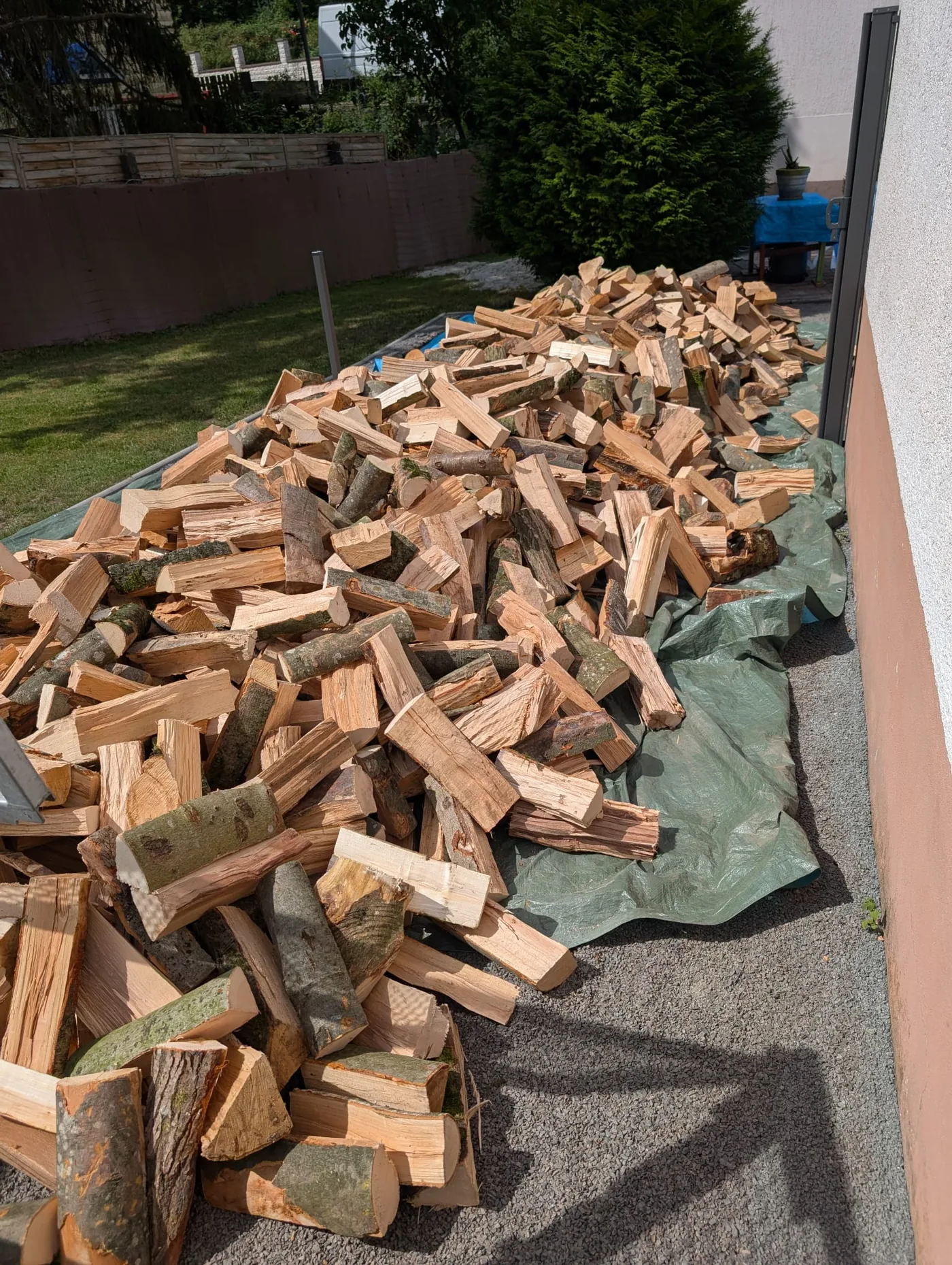 Frisch abgeladenes Brennholz auf einer Plane vor dem Haus eines Kunden